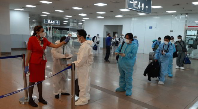 AirAsia ground crew performing mandatory temperature screening, while guests are lined up for check-in with physical distancing.