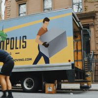 moving a house woman in blue shorts and black boots standing beside yellow and white truck during daytime