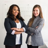 successful entrepreneur two women in suits standing beside wall