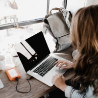 Start a Business Right girl wearing grey long-sleeved shirt using MacBook Pro on brown wooden table