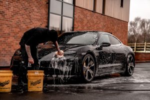 car shampoo man in black t-shirt and black pants doing water splash on black coupe during daytime