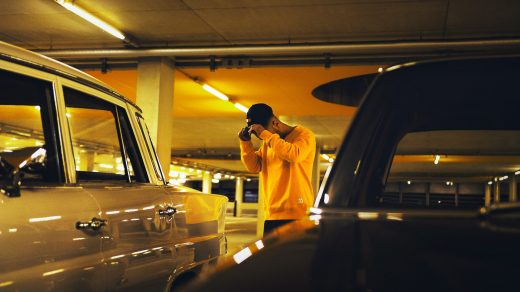 man holding cap standing between car on parking lot