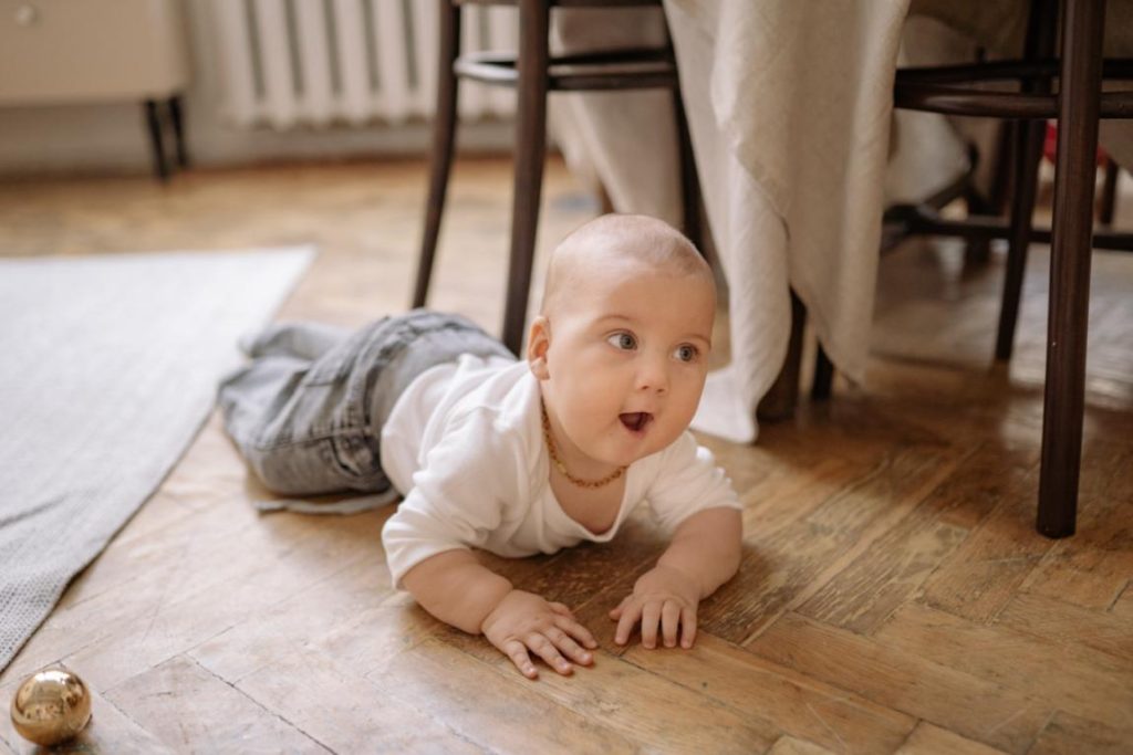 A baby crawling on the wooden floor.