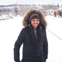 woman wearing coat standing on snow and smiling during daytime