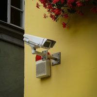 white and gray security camera mounted on yellow painted wall