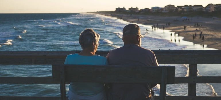 A retired couple sitting on a bench looking at the coastline