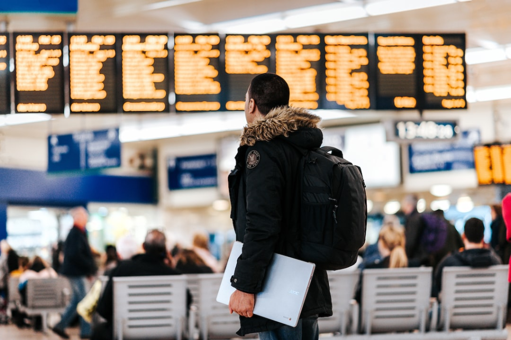 man standing inside airport looking at led flight schedule bulletin board