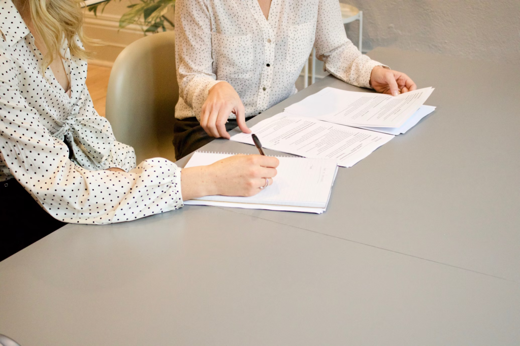woman signing on white paper beside woman about to touch the document