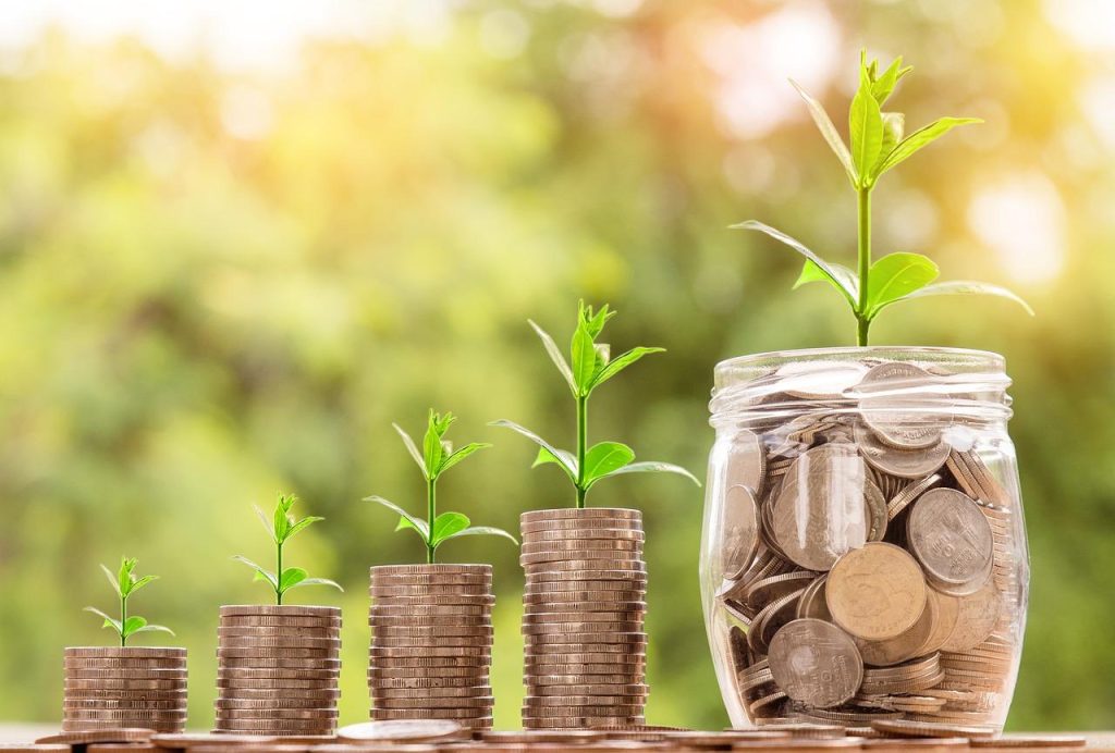 Stacks of coins increasing in height with green plant sprouts growing from the top.