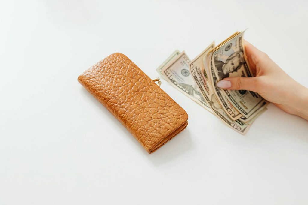 Understanding Assets And Liabilities 1 Assets And Liabilities- A hand counting American dollar bills next to a brown leather wallet on a white surface.