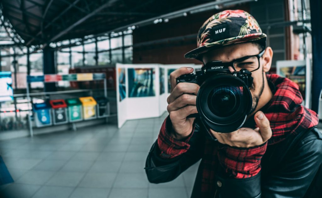 99 Ways For A Photographer To Make Money 1 A young adult photographer with a DSLR camera indoors, highlighting modern photography.