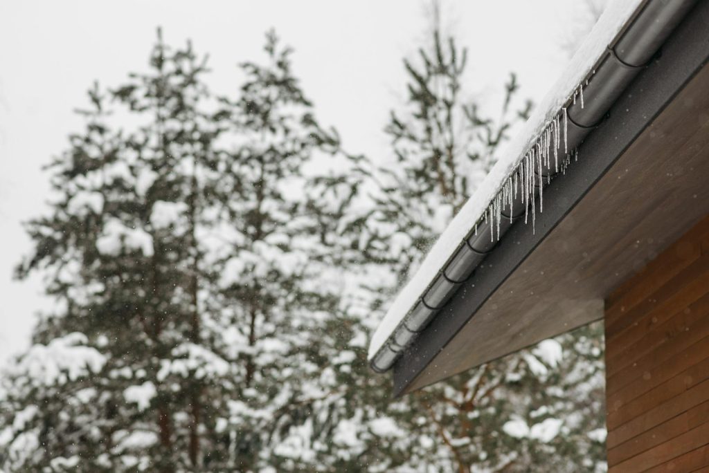 Keep Your Gutters Clean This Winter with Gutter Guards 1 Gutter Guards- Stunning winter scene of icicles hanging from a snow-covered roof with snowy pines in the background.