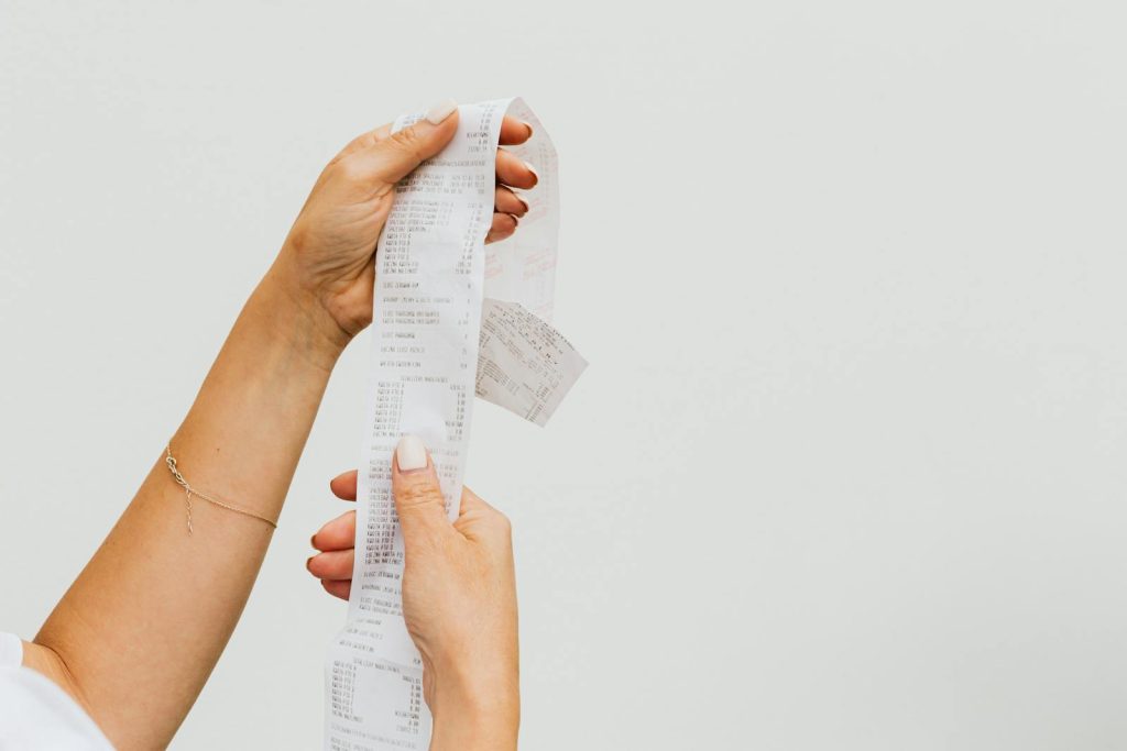 Cutting Your Grocery Bills in Half 1 A detailed view of a person holding a long shopping receipt against a plain background.